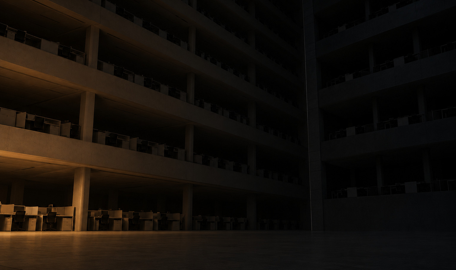 An immense empty office atrium at night, tiers of open-plan floors lined with identical empty desks rising past the top of the frame, a darker block of floors joined on at the right along a straight seam, and a weak amber light from the lower left catching only the nearest desks on the ground floor