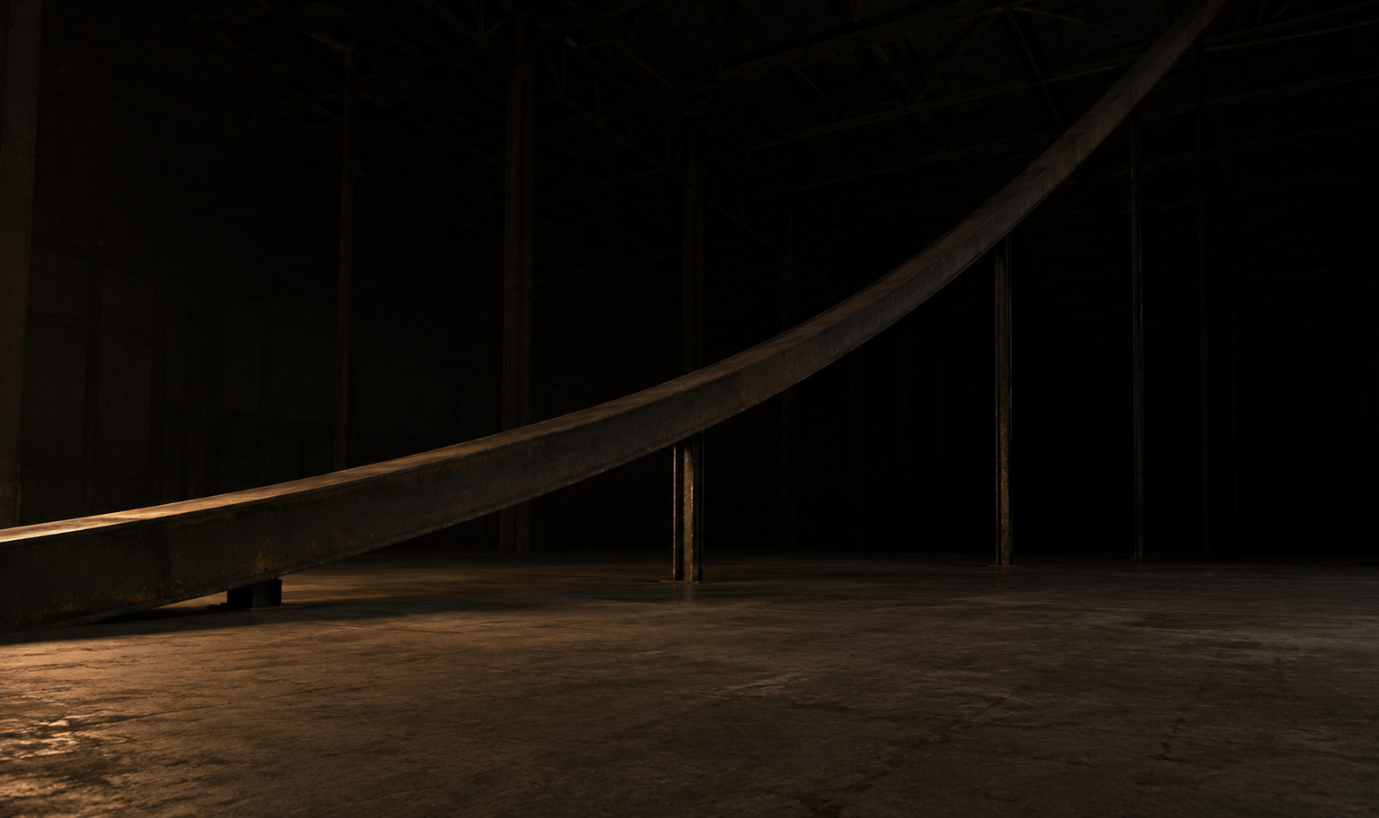 A single enormous steel beam rising from the concrete floor at the lower left of an unlit industrial hall and climbing away in a steepening curve, like the line of a graph, out of the top of the frame. Thin columns of increasing height hold it up, the farthest lost in darkness. A weak amber light from out of frame at the lower left reaches only the base of the beam and a strip of floor