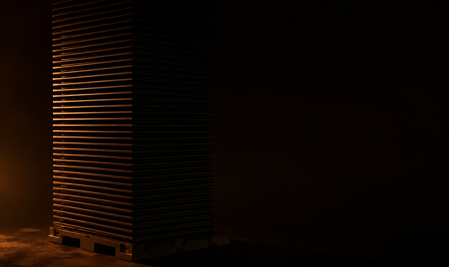 A tall stack of thin ceramic fuel cell plates in a dark field, lit along one edge by a single amber light