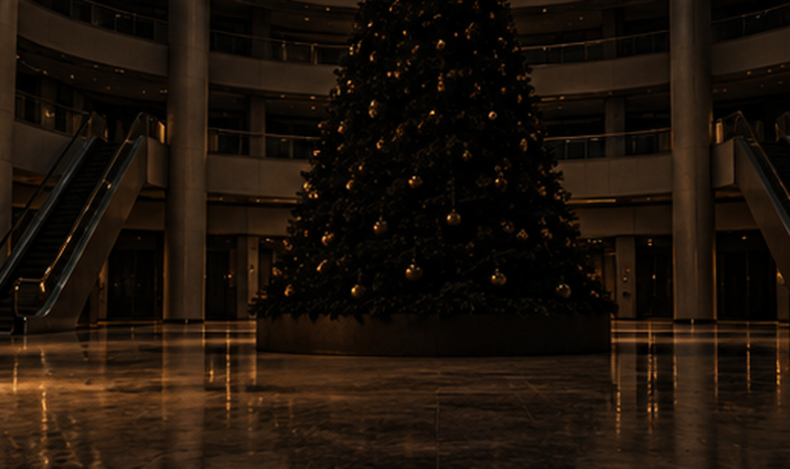 The atrium of an immense, empty shopping mall at night, a giant unlit holiday tree rising past the top of the frame between tiers of balconies with shuttered storefronts and stilled escalators, the far end lost in darkness, and a weak amber light from the lower left catching the lowest branches and a strip of polished floor