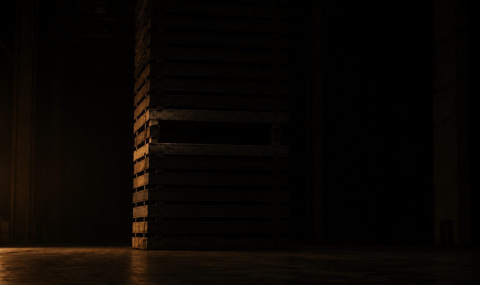 A stack of heavy pallets rising past the top of the frame in an unlit warehouse, with one run of them missing about a third of the way up to leave a void straight through the stack. A weak amber light from out of frame to the left reaches the near edges and the cut faces bounding the gap, while the rest of the hall falls away into black